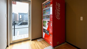 A Coca-Cola vending machine in a hallway with a sliding glass door leading outside. - HOTEL R9 The Yard Tomioka (Tomioka)