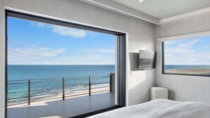 A modern hotel room with a large balcony overlooking the sea, a bed, and a TV mounted on the wall. - Beachfront Estate with Full-Time Staff, Airport Transfer & Beach/Fitness Club Ac (San Jose Del Cabo)