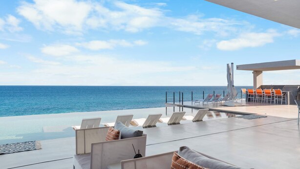A modern outdoor lounge area with a pool, lounge chairs, and a view of the ocean. - Beachfront Estate with Full-Time Staff, Airport Transfer & Beach/Fitness Club Ac (San Jose Del Cabo)