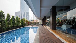 A rooftop pool with a wooden deck, glass balustrades, and a city view. - Cove The Day (Jakarta)