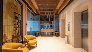 A modern lobby with a wooden ceiling, glass walls, and a seating area with yellow chairs. - Cove The Day (Jakarta)