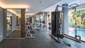 A modern gym with various exercise equipment, a large mirror, and a view of a swimming pool. - Cove The Day (Jakarta)