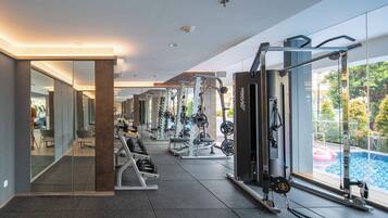 Un gimnasio moderno con equipo de ejercicio variado, un espejo grande y vistas a una piscina.