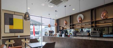 Interior moderno de una cafetería con barra, asientos y un ventanal grande.