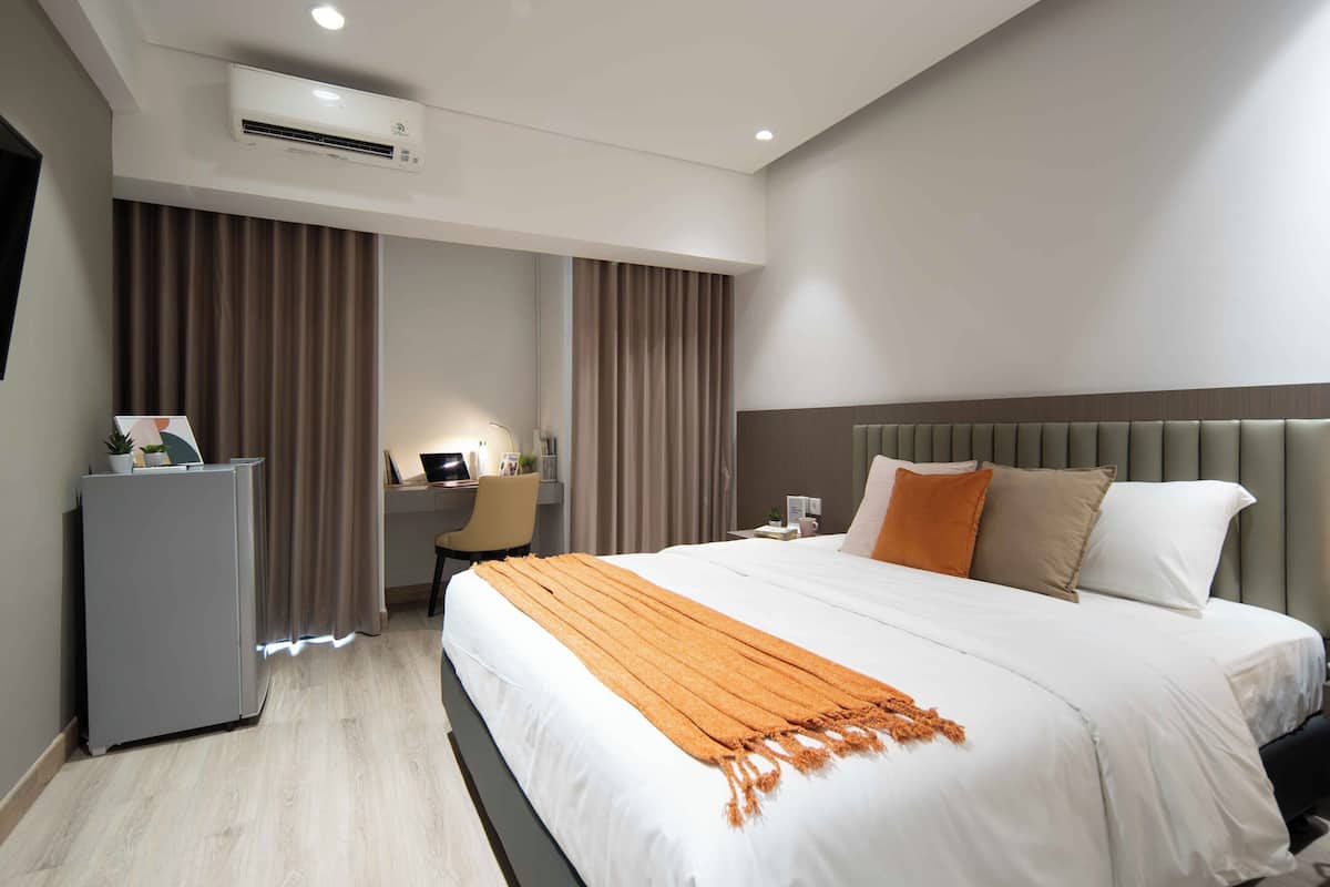 A modern hotel room with a bed, a desk, and an air conditioning unit.