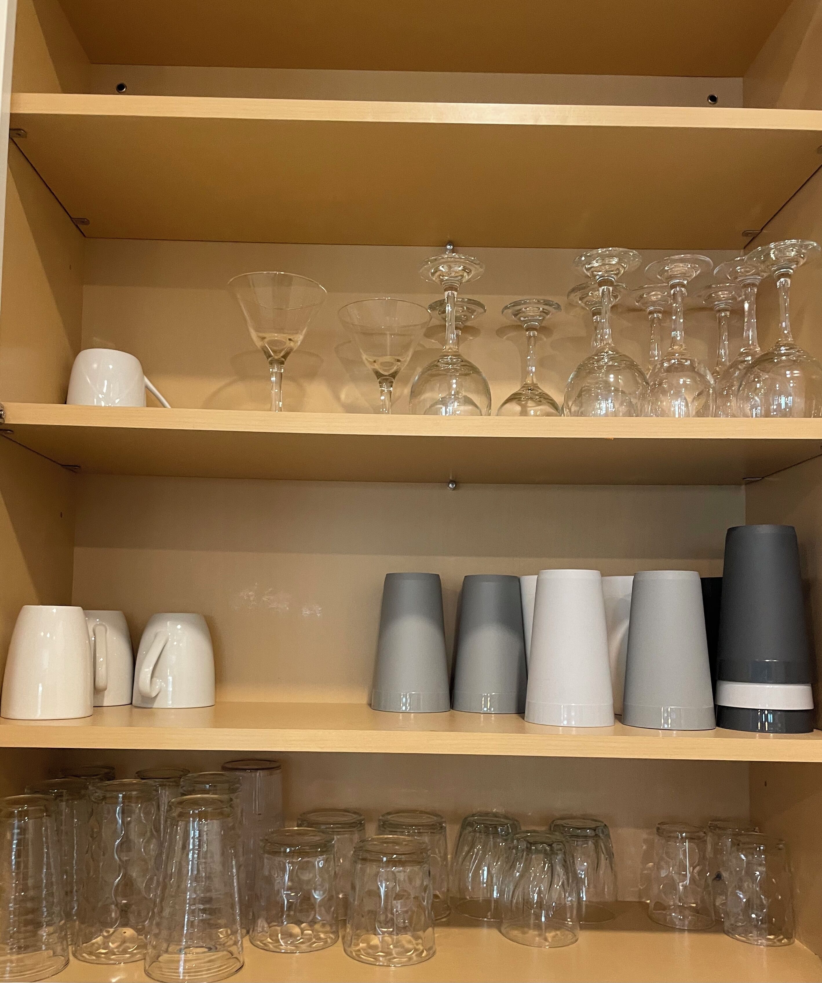 Un espace de rangement doté d’étagères contenant divers types de verrerie, notamment des verres à vin, des verres à cocktail et des mugs.