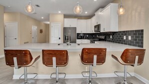 A modern kitchen with a central island, white cabinetry, and bar stools. - This retreat offers a stylish, resort experience with 9b5b and a private pool (Four Corners)
