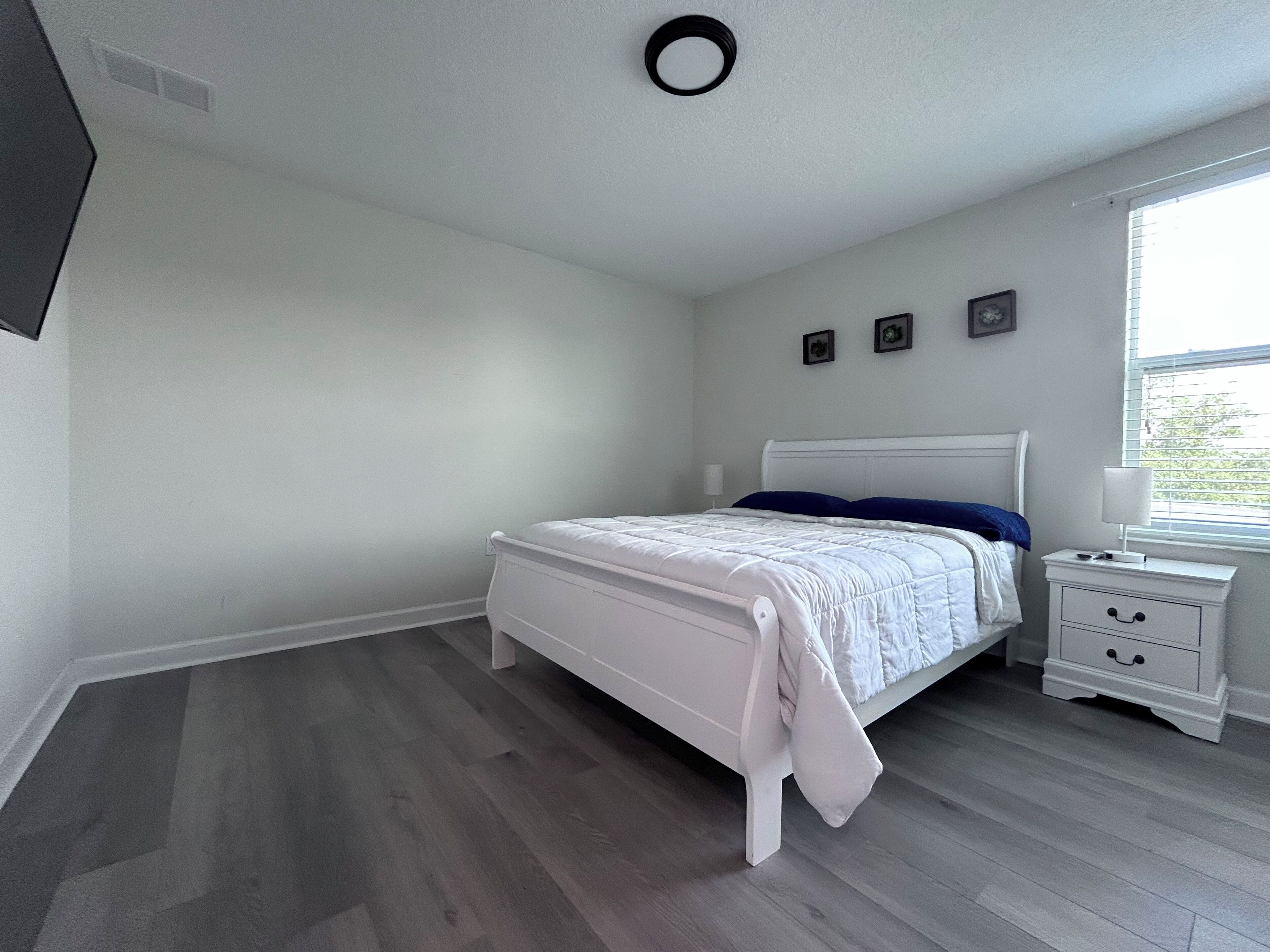 Een slaapkamer met een bed, nachtkastje en raam.