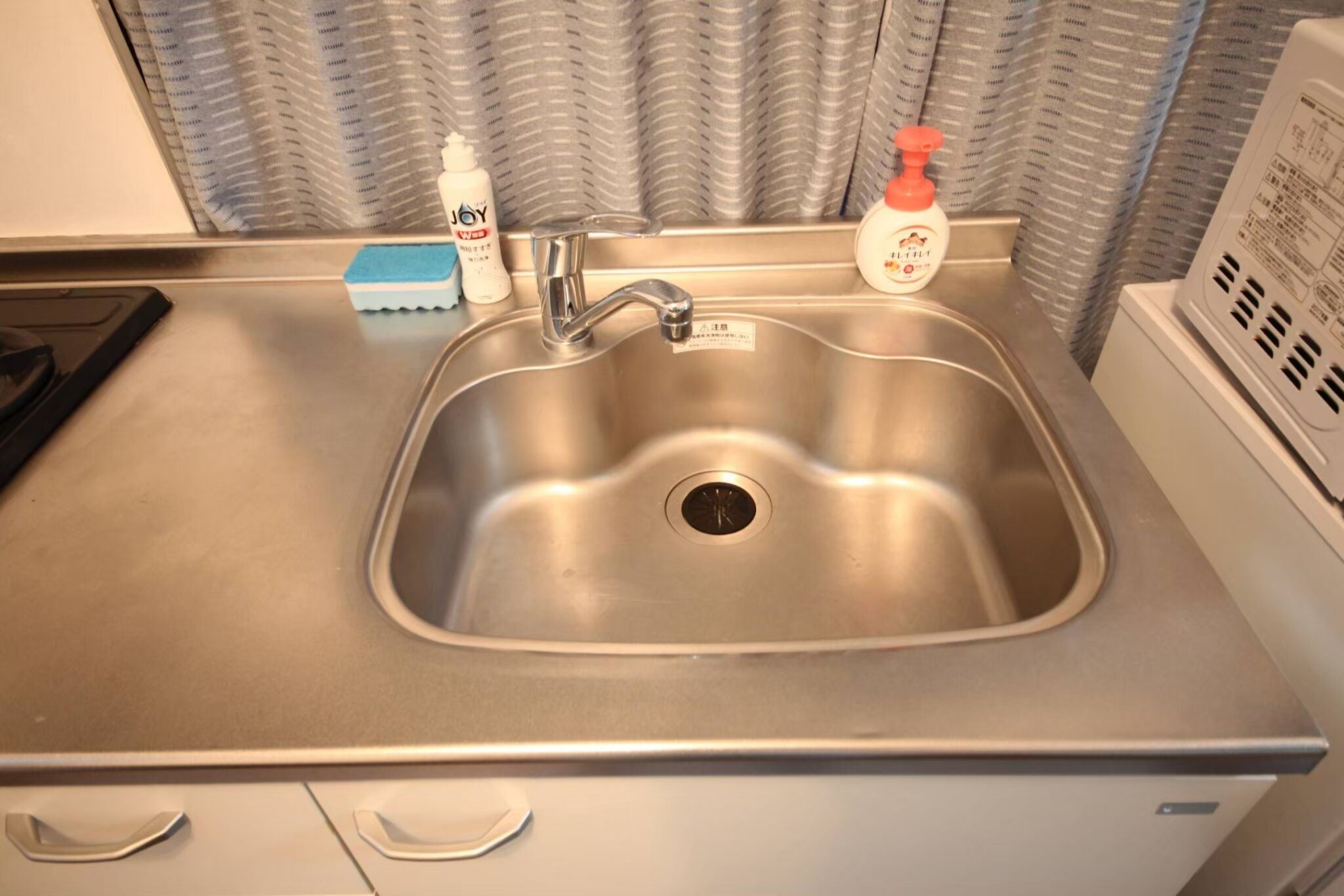 A stainless steel kitchen sink with a faucet, a soap dispenser, and a sponge.