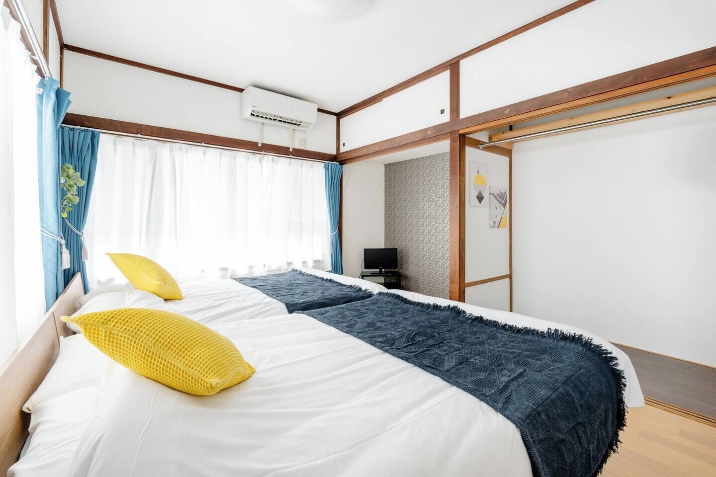 A bedroom with a bed, curtains, an air conditioning unit, a television, and a wall with a geometric pattern.