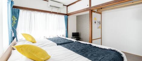 A bedroom with a bed, curtains, an air conditioning unit, a television, and a wall with a geometric pattern.