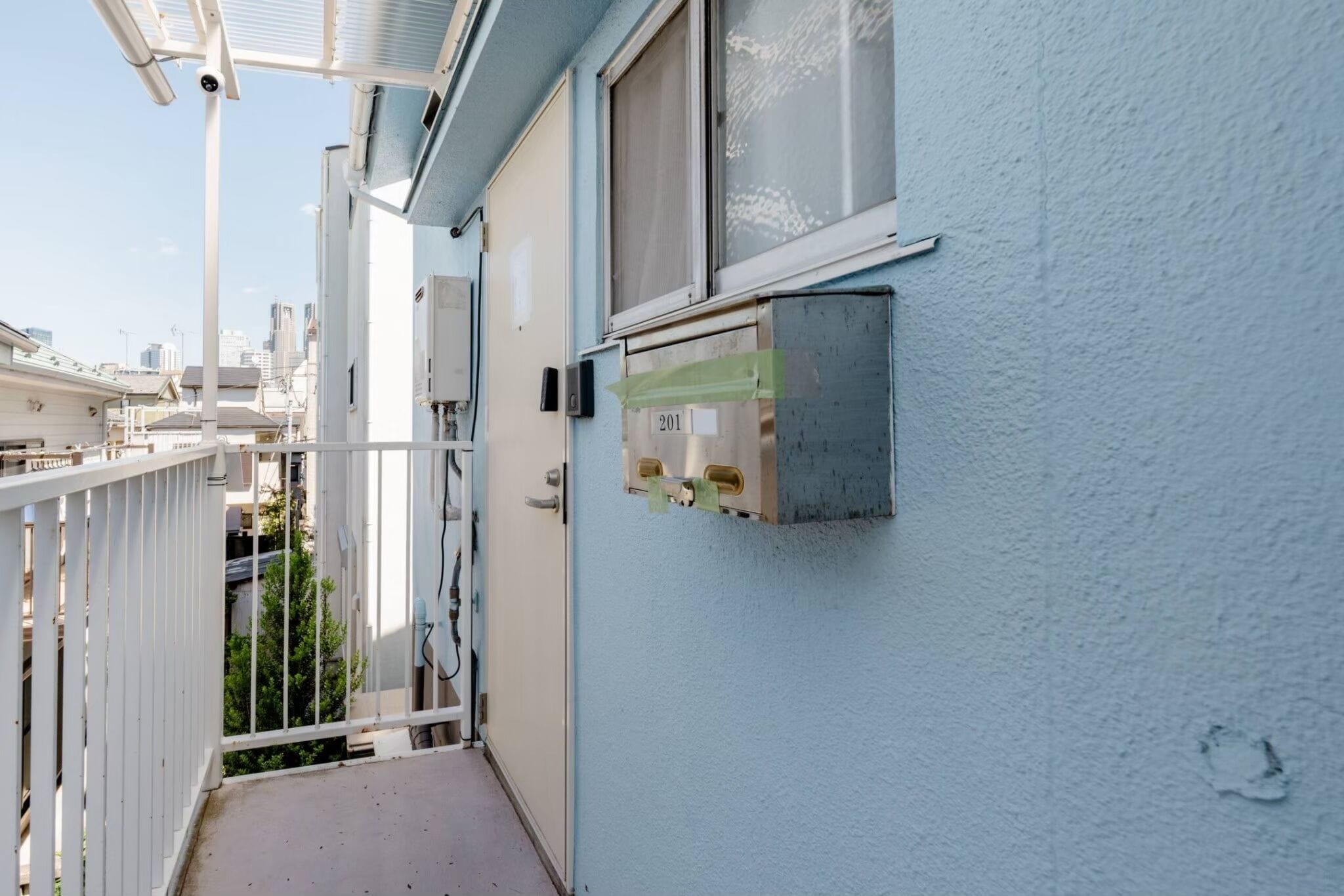 A narrow outdoor corridor with a white railing, a blue wall, and a window.