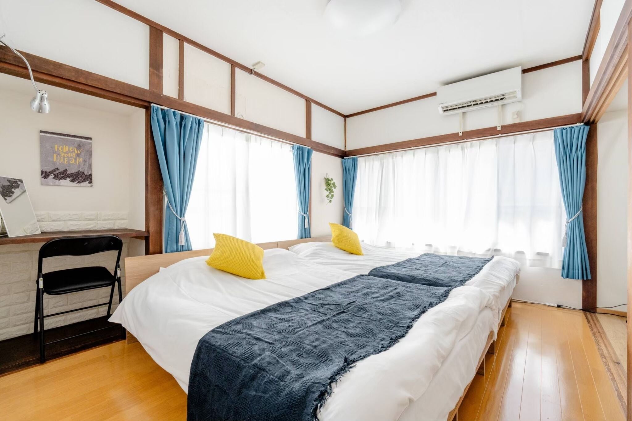 Habitación de hotel con una cama grande, vigas de madera, un escritorio con una silla y una ventana con cortinas azules.