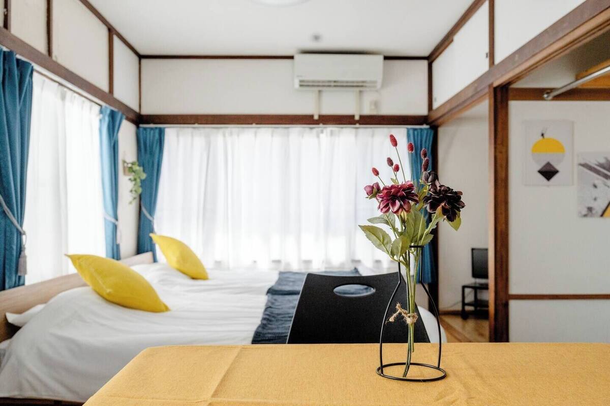 Ein Hotelzimmer mit einem Bett, einem Tisch mit Blumenvase und einem fenster mit Vorhängen.