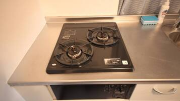 A kitchen with a gas stove, a sink, and a window with blinds.