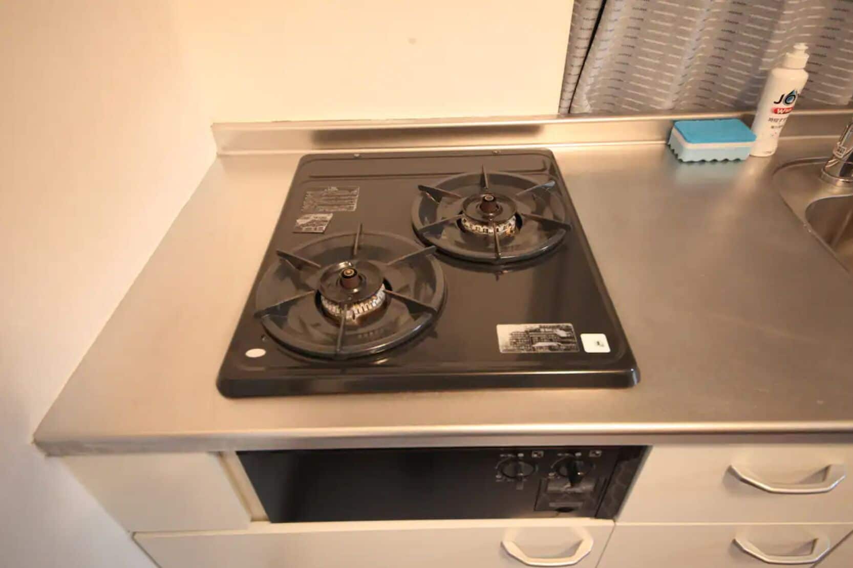 A kitchen with a stainless steel stove top, a sink, and a blue soap dish.