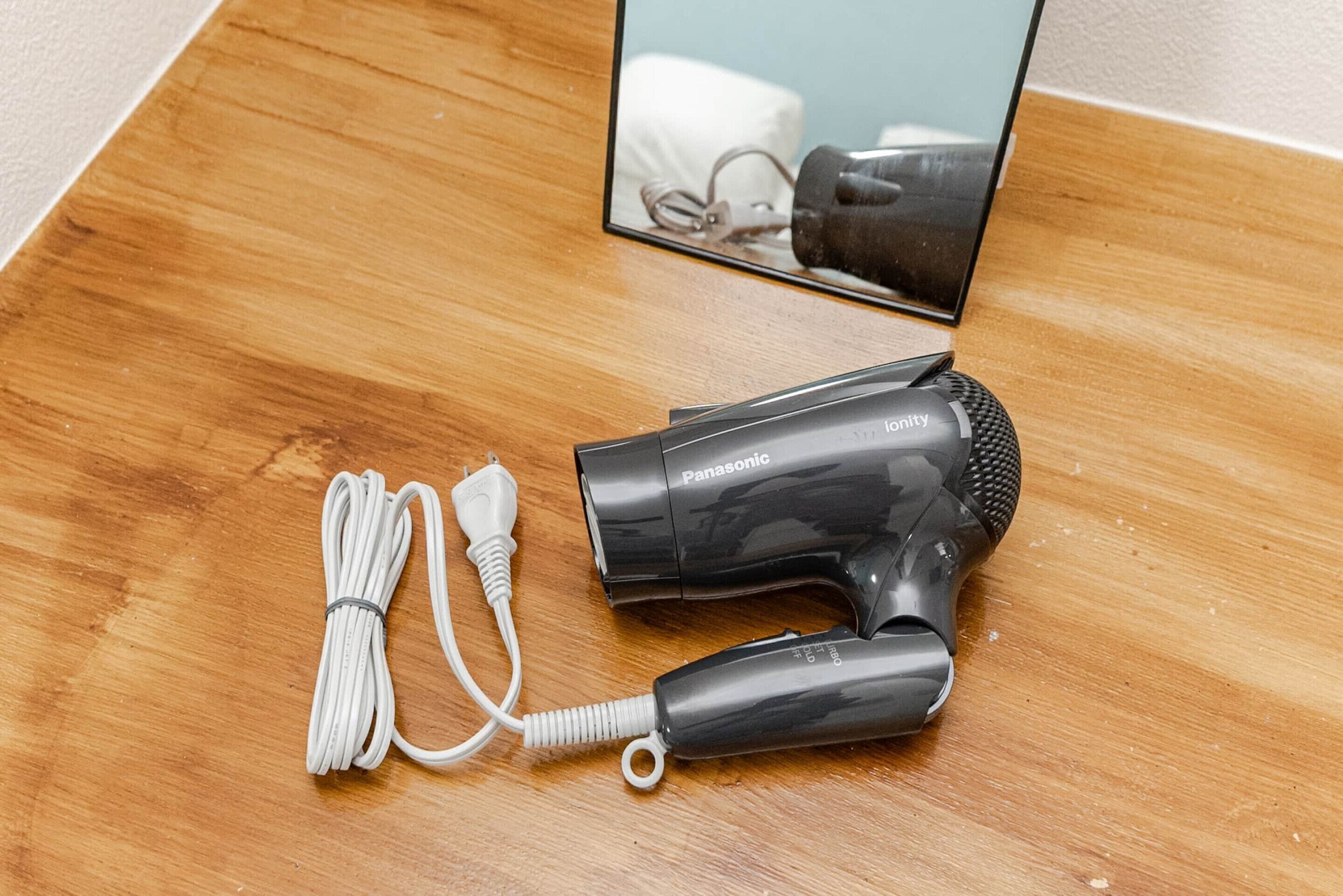Un secador de pelo Panasonic sobre una superficie de madera con un cable enrollado.