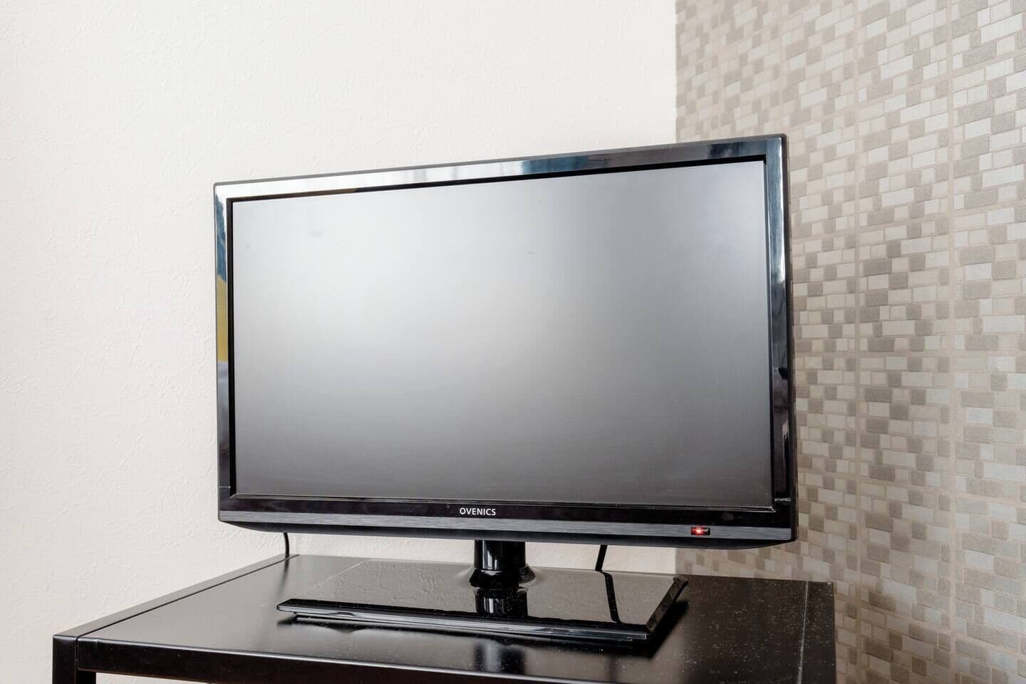 A flat-screen TV on a black stand against a wall with a mosaic tile pattern.