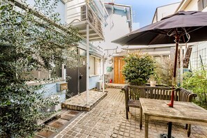 A courtyard with a table and chairs, a wooden door, and a potted plant. - Chelsea Hatsudai (Tokyo)
