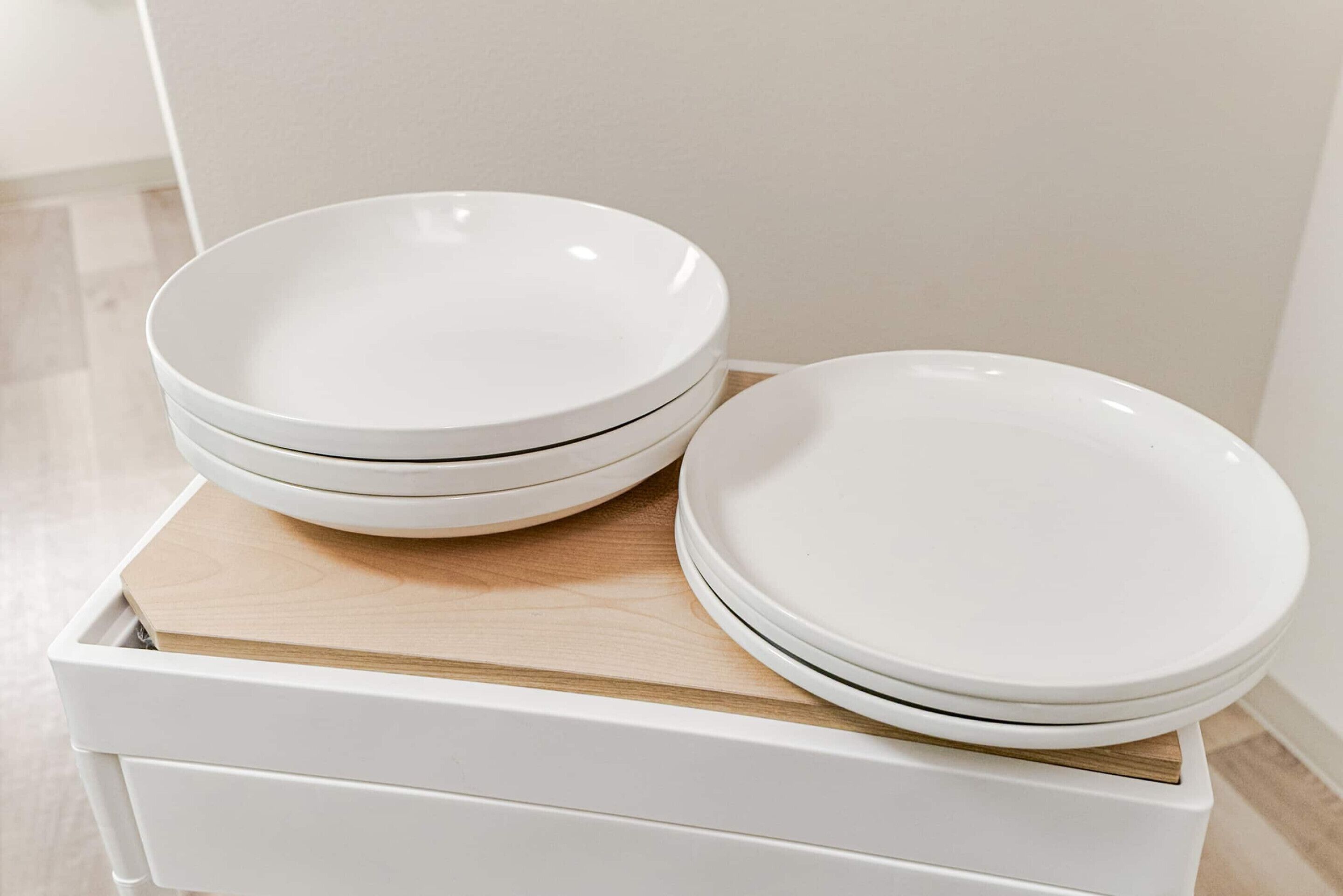 A stack of white bowls on a white tray with a wooden board.