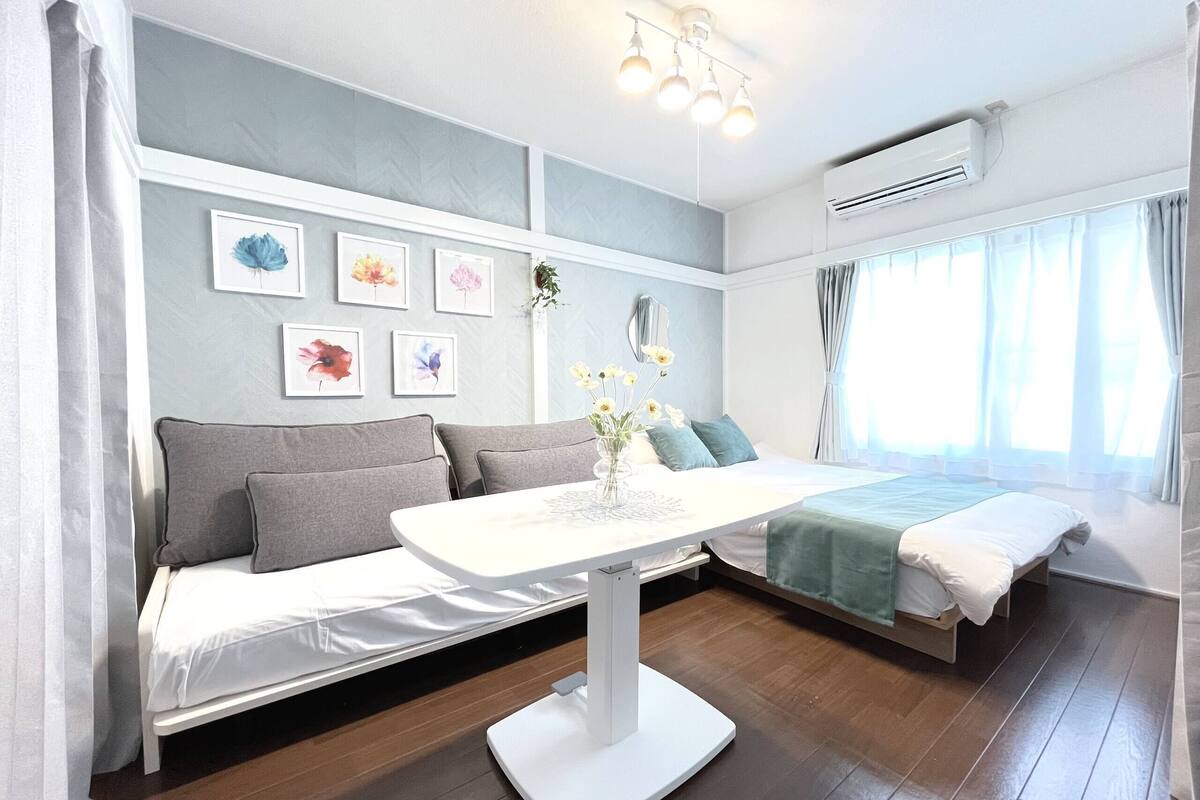 Ein modernes Schlafzimmer mit Schlafsofa, einem kleinen Tisch mit Blumenvase und einem Bett mit grüner Decke.
