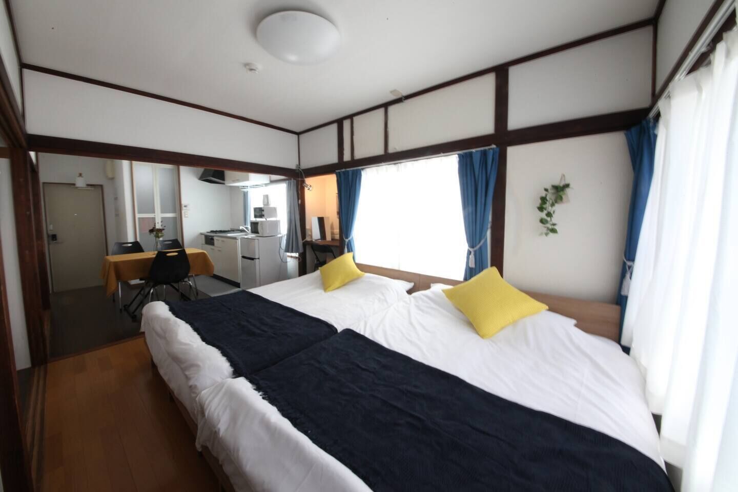 Habitación de hotel con dos camas, un escritorio, una silla, una kitchenette pequeña y una ventana con cortinas.