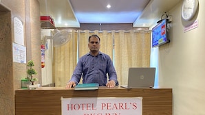 A reception desk at Hotel Pearl's BKC Inn with a laptop, a fan, and a sign indicating check-in and check-out times. - Hotel Pearls BKC Inn (Mumbai)