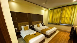 A hotel room with two beds, wooden flooring, a large window with yellow curtains, and a ceiling fan. - Hotel Pearls BKC Inn (Mumbai)