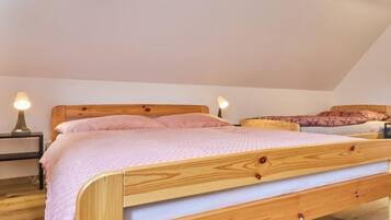 A single wooden bed in a room with a sloped ceiling, two bedside lamps, and a wooden floor.