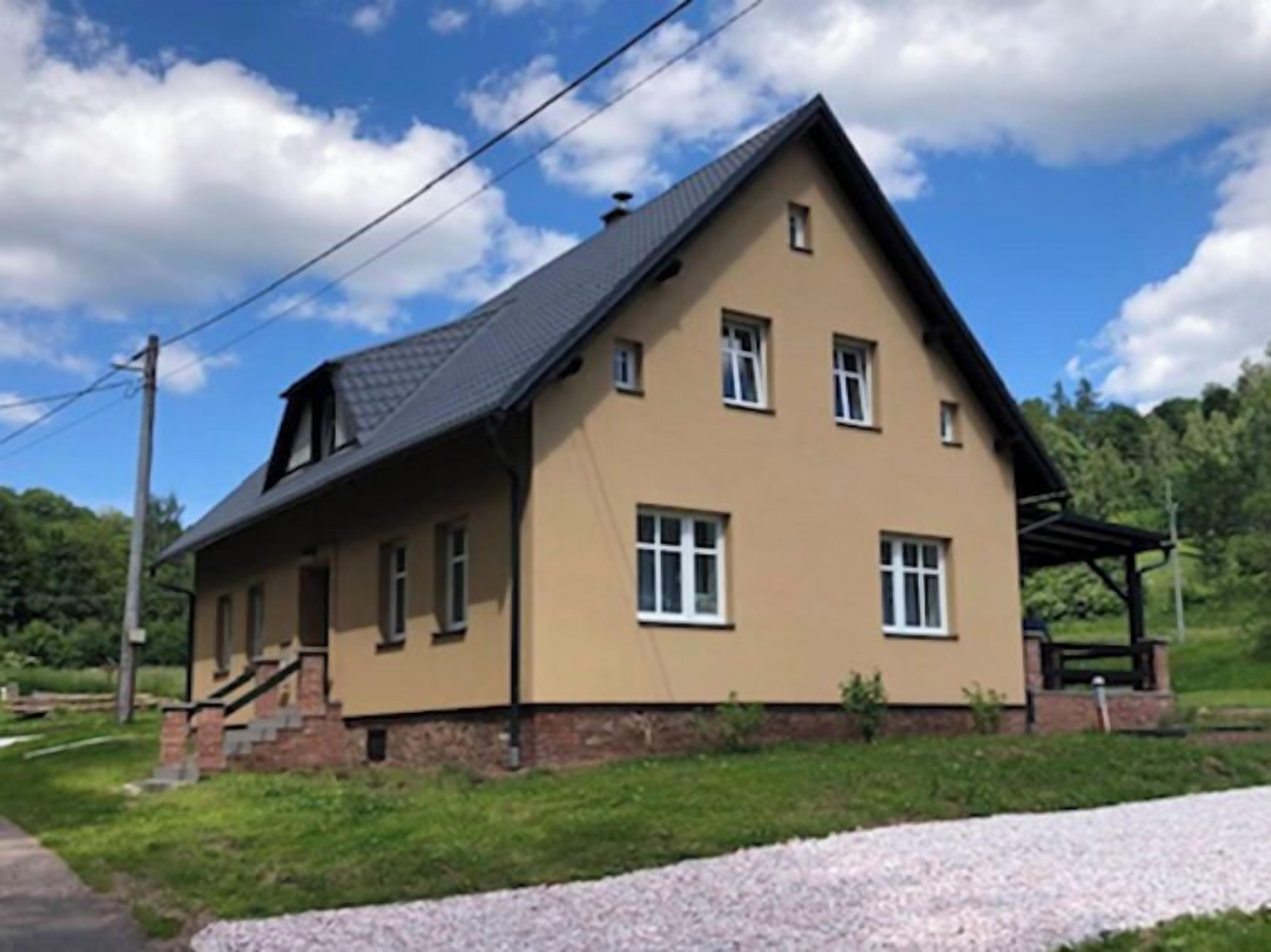 A two-story house with a sloped roof, a front porch, and a small garden area.