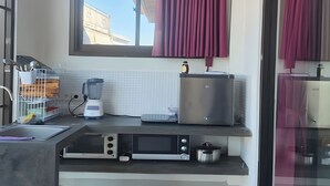 Una cocina moderna con horno empotrado, microondas y cafetera. Se ve una ventana con cortinas, un lavamanos y una encimera con escurreplatos.