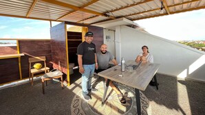 Un espacio al aire libre moderno con una mesa y sillas de madera, una silla amarilla y una botella de agua metálica sobre la mesa.