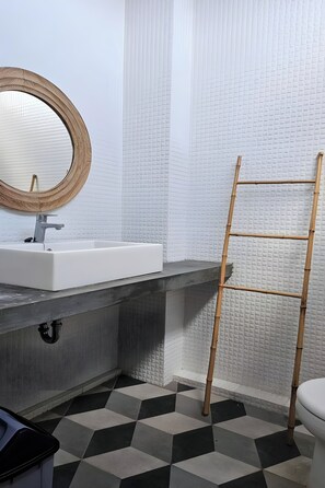 Une salle de bain avec un lavabo blanc, un miroir rond et des murs carrelés.