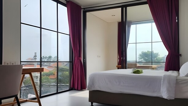 Un dormitorio moderno con una cama grande, un escritorio y vistas de la ciudad a través de ventanales.