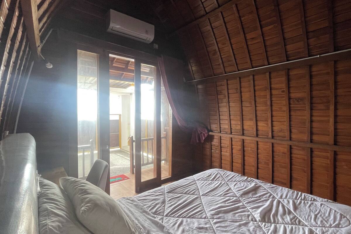A room with a bed, wooden walls, a sliding glass door, and an air conditioning unit.