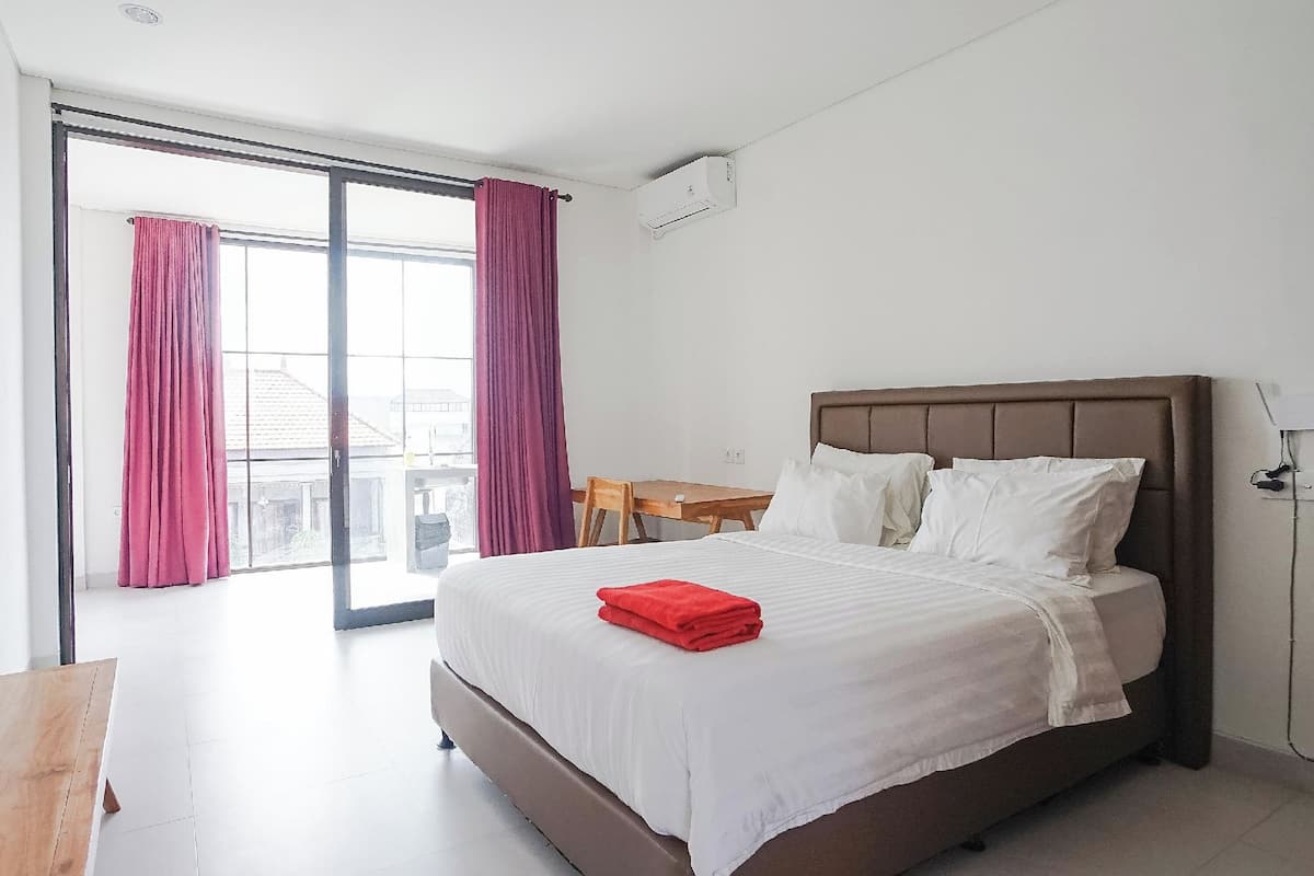 A hotel room with a large bed, a wooden desk, and a view through a sliding glass door.