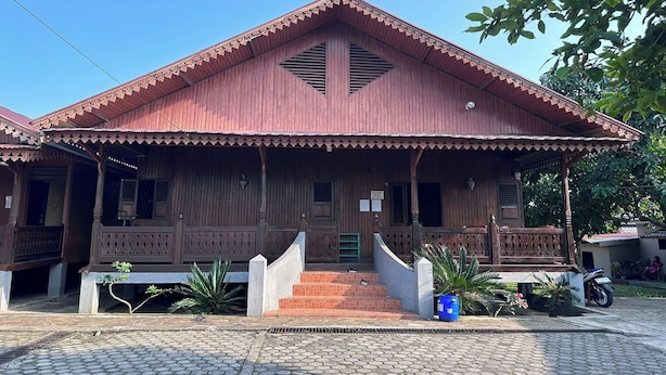 A wooden house with a porch, steps leading to the entrance, and a motorcycle parked outside. - Channes Guest House Syariah (Bengkulu)