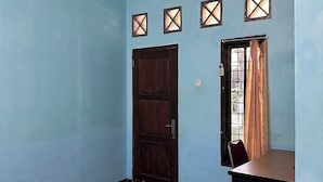 A room with a tiled floor, a wooden door, a desk, and an air conditioning unit. - Channes Guest House Syariah (Bengkulu)