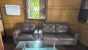 A room with a brown leather sofa, a glass coffee table with a ship model, and a window with a metal grid. - Channes Guest House Syariah (Bengkulu)