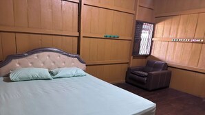 A bedroom with a bed, a chair, wooden panel walls, and a window with a metal grid. - Channes Guest House Syariah (Bengkulu)