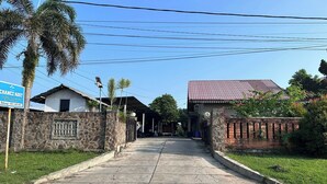 A paved pathway leading to a building with a red-tiled roof, surrounded by greenery and a stone wall. - Channes Guest House Syariah (Bengkulu)