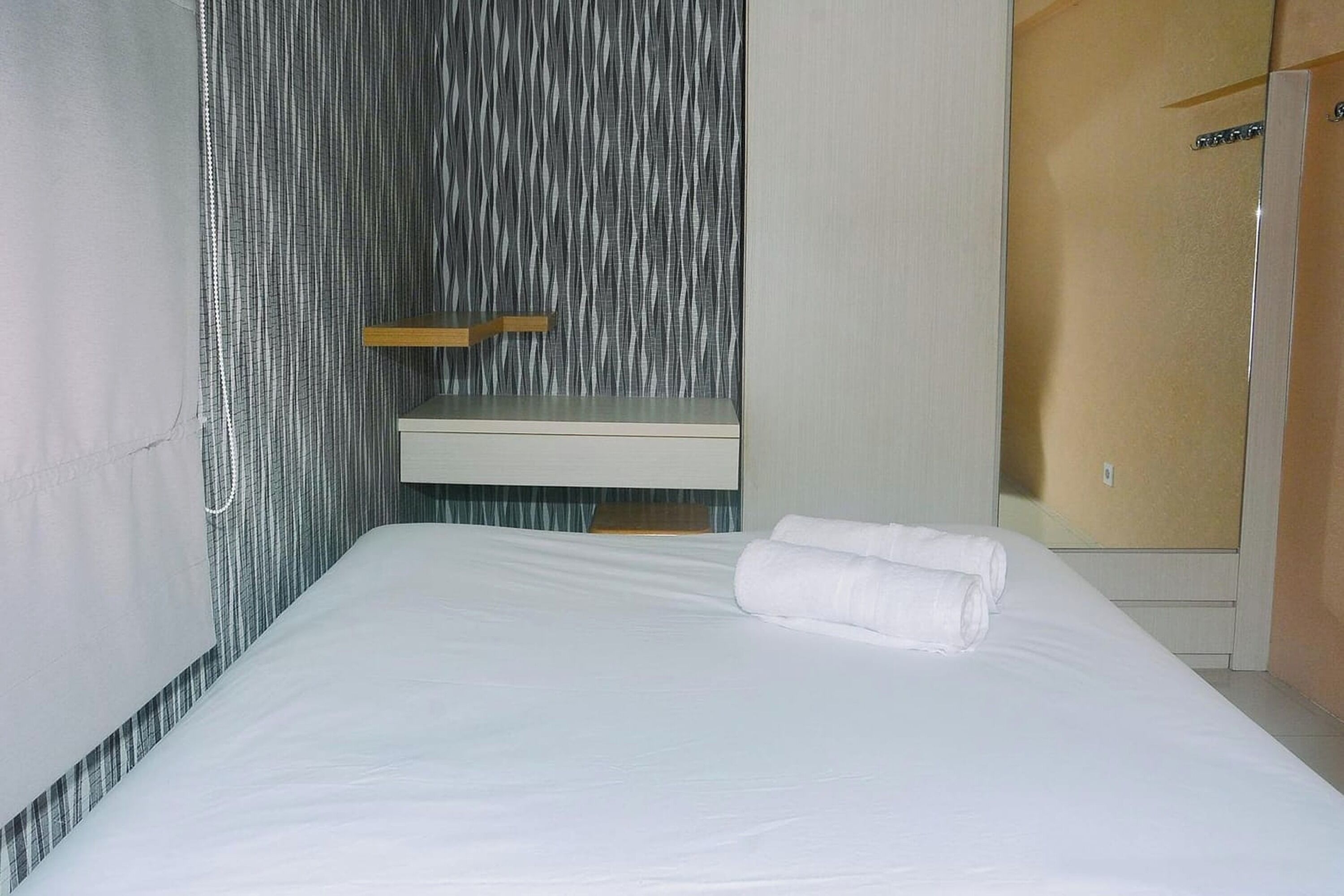 Ett hotellrum med en säng, ett litet sängbord, en spegel och en garderob.