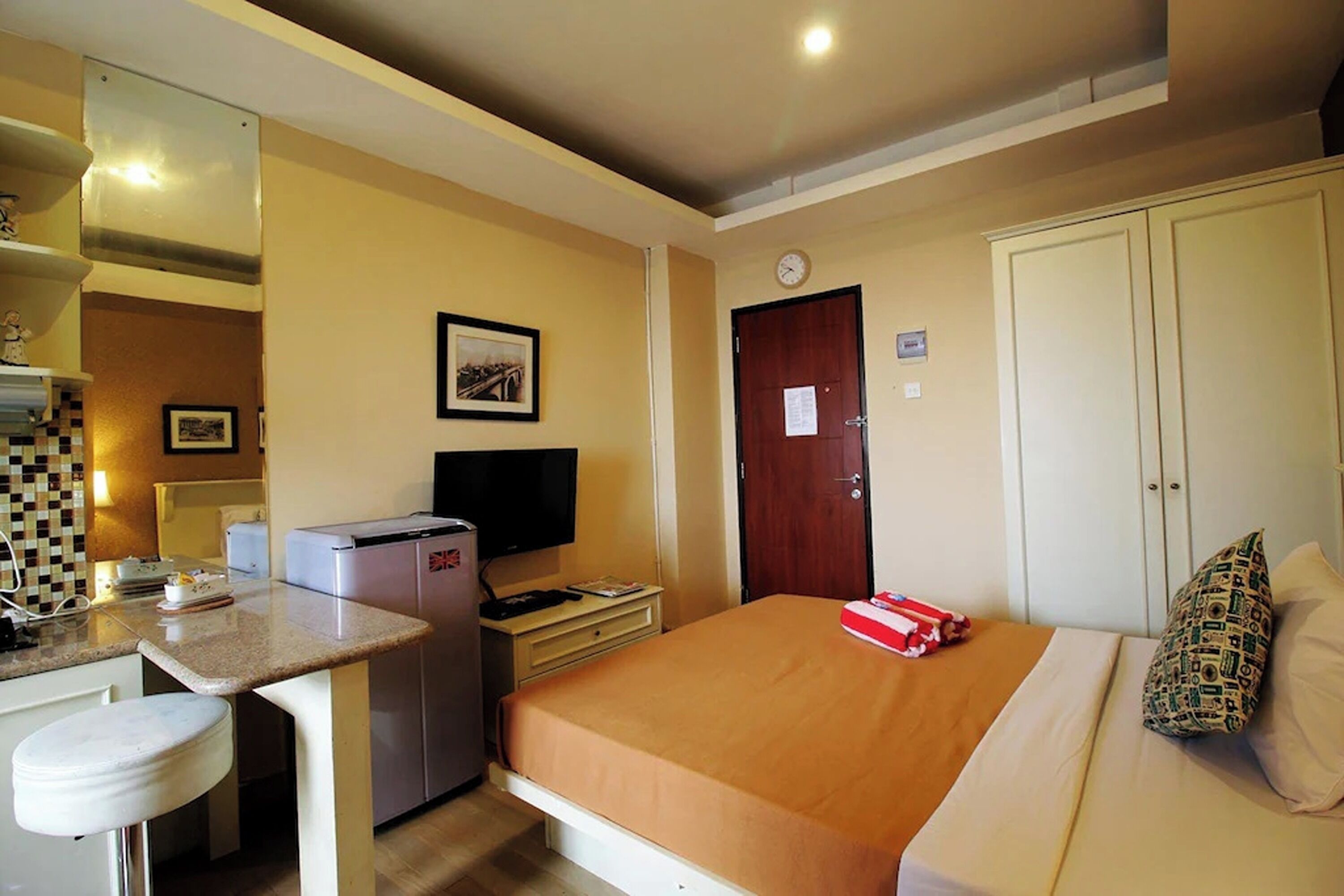 A compact hotel room with a bed, a small desk with a television, a refrigerator, and a bathroom with a toilet.