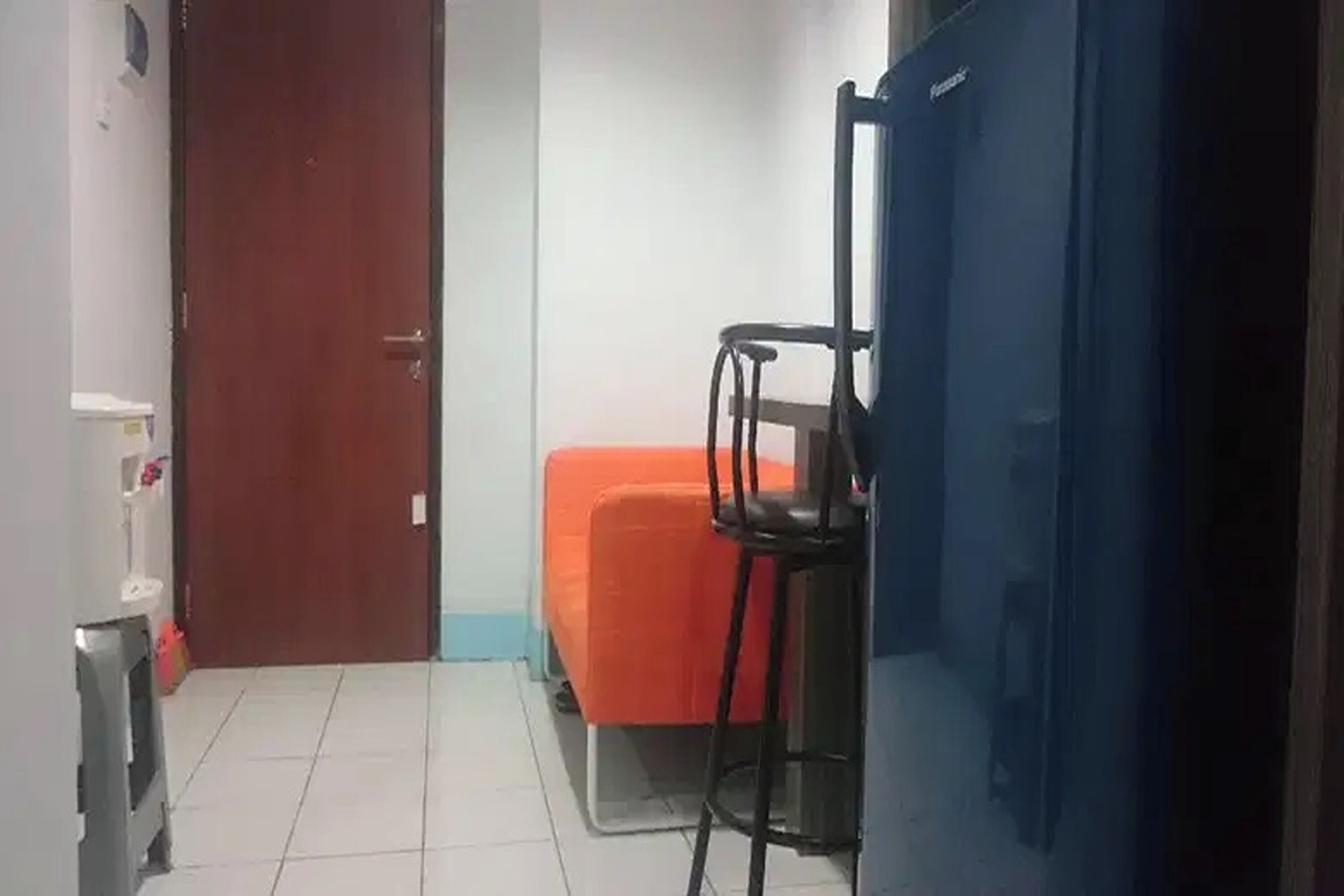 Ein kleines Zimmer mit einem Bett, einem Sessel, einem blauen Schrank und einer Tür.