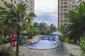 A swimming pool area with a slide, surrounded by palm trees and a playground. - Kebagusan City Apartment By Dina Rooms (Jakarta)