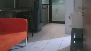 A compact kitchen with a red sofa, a refrigerator, and a small stool.
