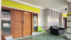 A lobby with wooden double doors, a green chair, a black sofa, and a tiled floor.