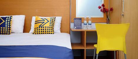 A hotel room with a bed, a desk, a chair, and a mirror.