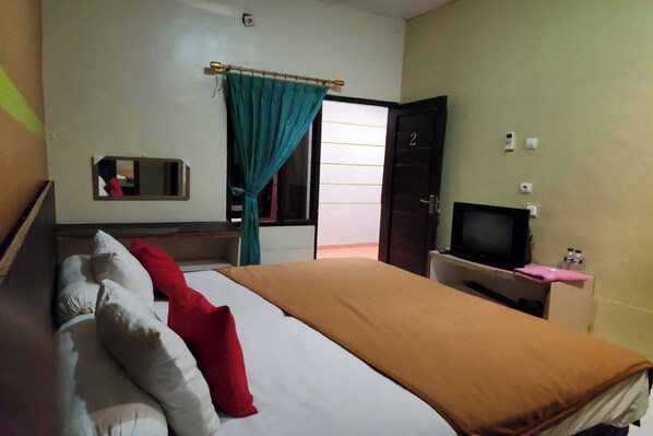 A hotel room with a bed, a television, a desk, and a door. - Griya Sakura Syariah near UMS (Colomadu)
