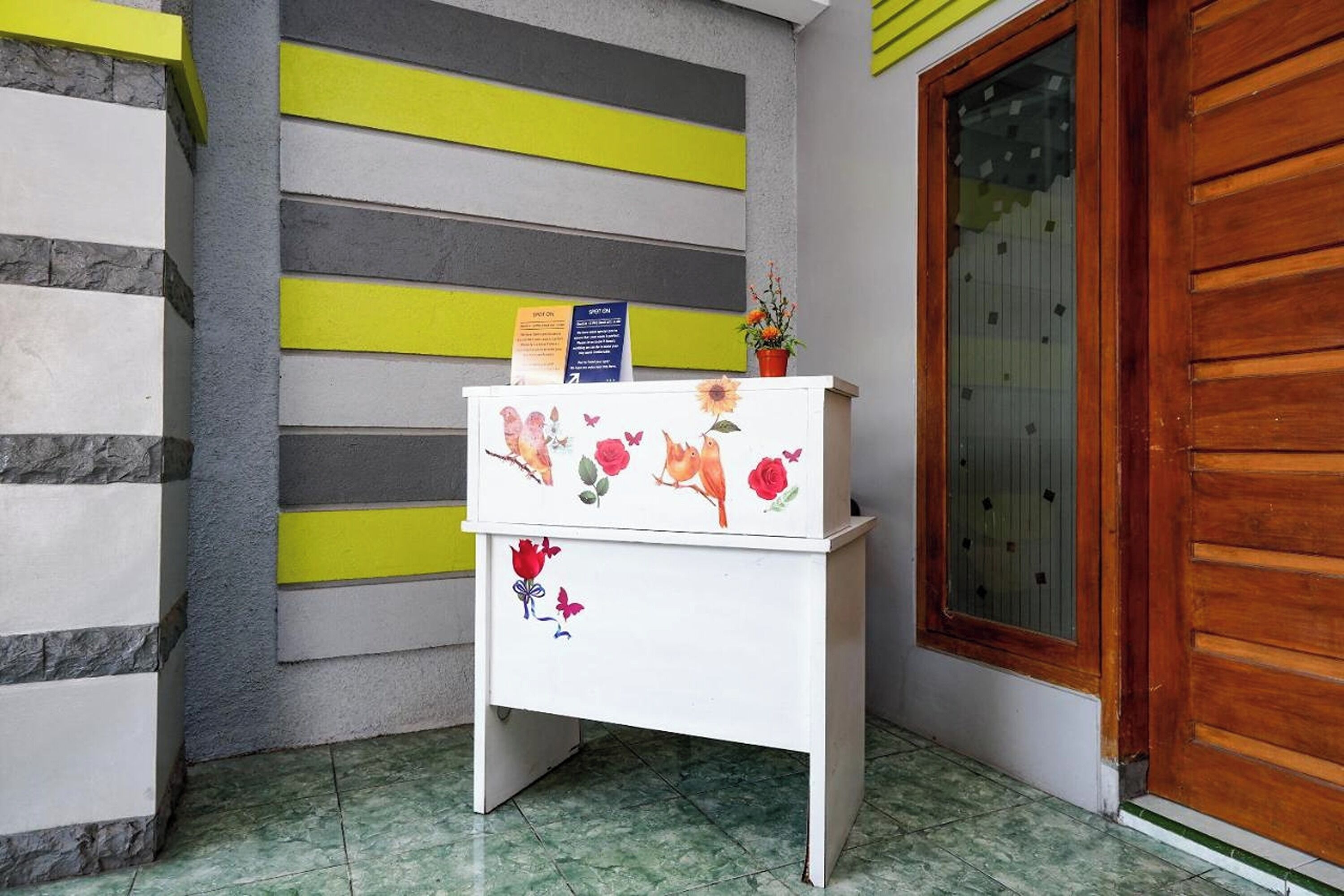 Un comptoir d’accueil orné de motifs floraux, une porte en bois et un mur à rayures horizontales.